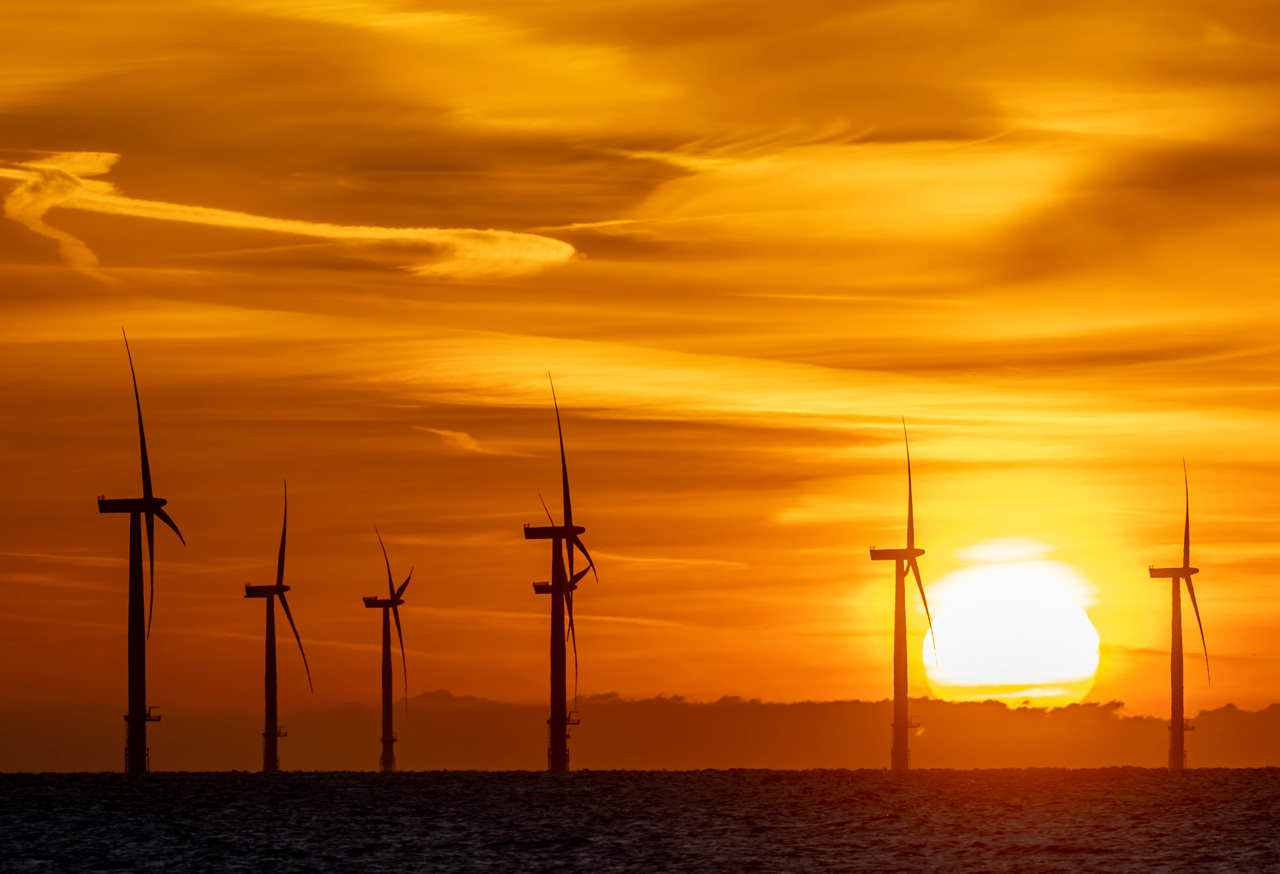 Offshore wind turbines against a an orange sky at sunset